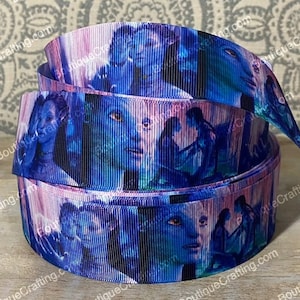 May include: A roll of blue and purple ribbon featuring images of characters from the movie Avatar. The ribbon has a vertical striped pattern and the images are of the Na'vi people. The ribbon is suitable for crafting and decorative purposes.