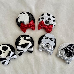 May include: A collection of six sequined hair clips featuring various character designs. The clips include a dalmatian-inspired design with a red bow, a Jack Skellington design with a black and white bow, and a Stormtrooper design with a silver bow.