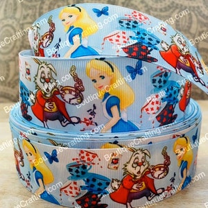 Puede incluir: Cinta azul y blanca con un patrón repetido de personajes de Alicia en el País de las Maravillas, incluyendo a Alicia, el Conejo Blanco y tazas de té. La cinta está hecha de grosgrain y tiene un acabado satinado.