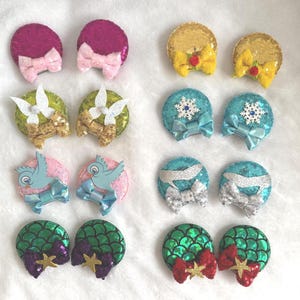 May include: A collection of colorful, sequined hair clips in various designs. The clips feature bows, birds, snowflakes, and mermaid scales in shades of pink, gold, blue, green, and silver. Each clip is approximately 2 inches in diameter.