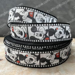 May include: Black and white ribbon with a repeated pattern of Mickey Mouse in film strip frames. The ribbon is 1.5 inches wide.