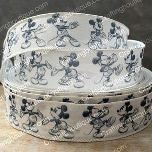 May include: Three rolls of white ribbon with a black and white print of Mickey Mouse. The ribbon is perfect for crafting and decorating.