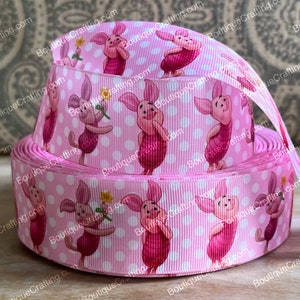 May include: Pink ribbon with a white polka dot pattern featuring a repeated image of Piglet from Winnie the Pooh. The ribbon is folded in a stack of three layers.