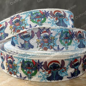 May include: White ribbon featuring a repeating pattern of the character Stitch in Christmas attire, surrounded by snowflakes. The ribbon is rolled up, showcasing the design. The text "CraftingBoutique.com" is printed along the edges.