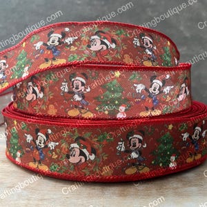 May include: Red and green Christmas ribbon with a repeating pattern of Mickey Mouse and Minnie Mouse wearing Santa hats. The ribbon features a red border and a white background with green Christmas trees.