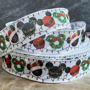 May include: White satin ribbon with a repeating pattern of Mickey Mouse wearing a Santa hat, a Christmas wreath, and colorful Christmas lights.