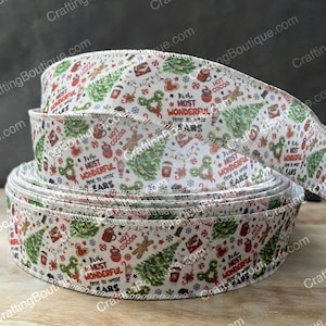 May include: White Christmas ribbon with a red and green print. The ribbon features a repeating pattern of Christmas trees, ornaments, and the text "It's the most wonderful time to wear ears".