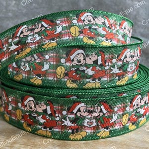 May include: A roll of green Christmas ribbon featuring a repeating pattern of Mickey Mouse and Minnie Mouse in Santa hats. The ribbon has a plaid background with red and white accents. The edges are finished with a green trim.