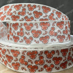 May include: White ribbon with a repeating pattern of red Mickey Mouse heads and candy canes. The ribbon is tightly wound in a roll, showcasing the festive design. The ribbon is perfect for holiday crafts and gift wrapping.