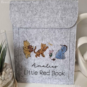 May include: Grey felt book cover featuring Winnie the Pooh and his friends. The cover is personalised with the name "Amales" and the text "Little Red Book".