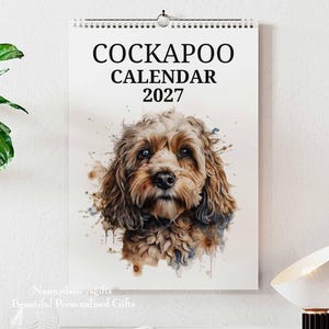 May include: A wall calendar for the year 2027 featuring the text COCKAPOO CALENDAR 2027 at the top. The centre of the page displays a watercolour-style illustration of a brown, curly-haired dog with dark eyes and a black nose on a white background.