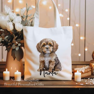 May include: A cream-coloured tote bag with a watercolour illustration of a brown and tan puppy, and the name "Marla" in black script. The bag has two handles and is on a wooden surface.
