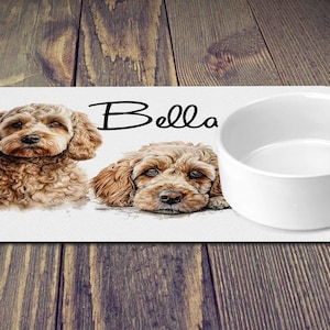 May include: White personalised dog bowl mat with two brown and white dogs and the name "Bella" printed on it.