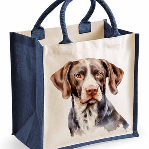 May include: A brown and white dog with brown eyes is printed on a white canvas tote bag. The bag has navy blue handles and trim.