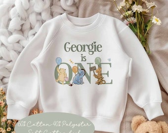 May include: White sweatshirt with a green 'ONE' graphic featuring Winnie the Pooh and his friends. The text 'Georgie is ONE' is printed above the graphic. The sweatshirt is made of 60% cotton and 40% polyester.