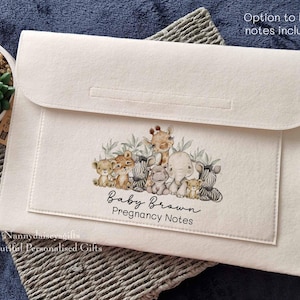 May include: A white felt folder with a zip closure. The folder features a design of a group of safari animals, including a giraffe, elephant, rhino, and lion. The text "Baby Brown Pregnancy Notes" is printed on the folder.