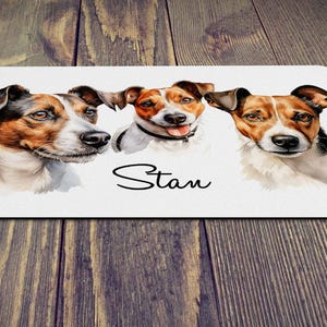 May include: A rectangular white mat with three Jack Russell Terrier portraits. The dogs are painted in watercolour, with brown and black markings. The name "Stan" is written in cursive below.