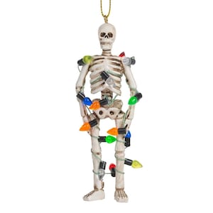 May include: A hanging skeleton ornament featuring an off-white bone-colored finish, wrapped in a string of multi-colored miniature light bulbs in shades of red, green, blue, orange, and clear, suspended by a thin gold-colored hanging cord.
