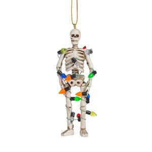 May include: A white skeleton ornament with a gold string for hanging. The skeleton is decorated with a string of colorful Christmas lights. The lights are in various colors, including red, green, orange, and blue. A festive Halloween or Christmas decoration.