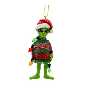 May include: Green alien Christmas ornament wearing a red Santa hat and tangled in Christmas lights.