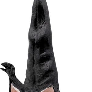 May include: A black bat ornament hanging upside down by a gold string. The bat has large, light pink ears, red eyes, and an open mouth revealing white teeth. Its wings are partially spread, and its body features a textured, matte black finish.