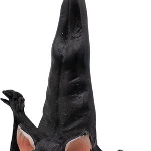 May include: A black hanging bat ornament with large pink ears, red eyes, and an open mouth showing white teeth. The bat is suspended by a thin gold string attached to a metal loop at the top of its head, featuring a textured body and wings.