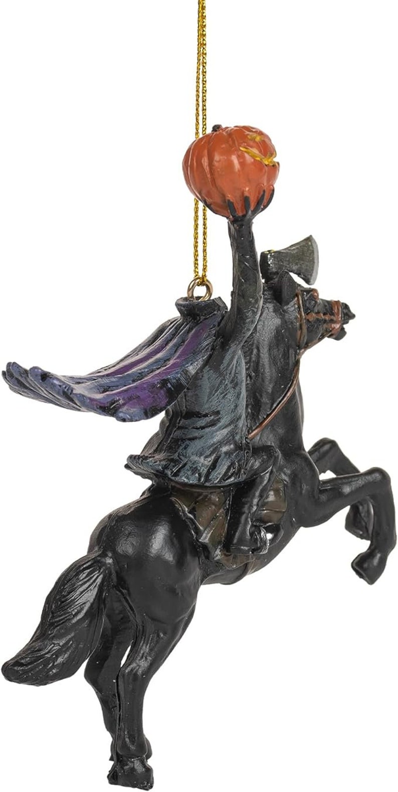 Puede incluir: Un adorno colgante que representa a un jinete sin cabeza sobre un caballo negro. El jinete viste un abrigo oscuro con reflejos morados y sostiene una calabaza naranja en alto. Un hacha es visible sobre el lomo del caballo.
