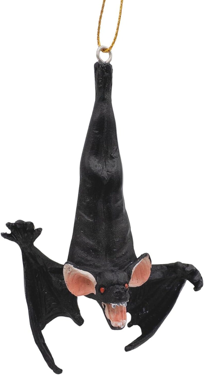 May include: A black hanging bat ornament with outstretched wings, pink inner ears, red eyes, and an open mouth showing white teeth. The bat is suspended by a thin gold string attached to a metal loop at the top of its head, hanging in a vertical position.