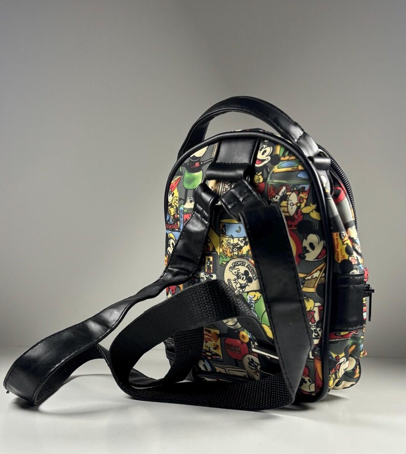 Puede incluir: Una mochila peque&ntilde;a con un estampado colorido de paneles de c&oacute;mic vintage de Mickey Mouse. El bolso cuenta con ribetes de piel sint&eacute;tica negra, un asa superior, correas de hombro ajustables de cinta negra y un cierre de cremallera lateral.