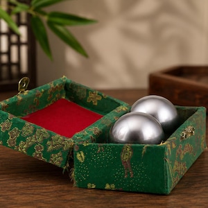 Peut inclure: Deux sphères métalliques argentées polies reposant à l'intérieur d'une boîte rectangulaire recouverte de tissu vert. La boîte présente un couvercle à charnière avec un loquet en métal doré et une doublure intérieure en velours rouge vif.