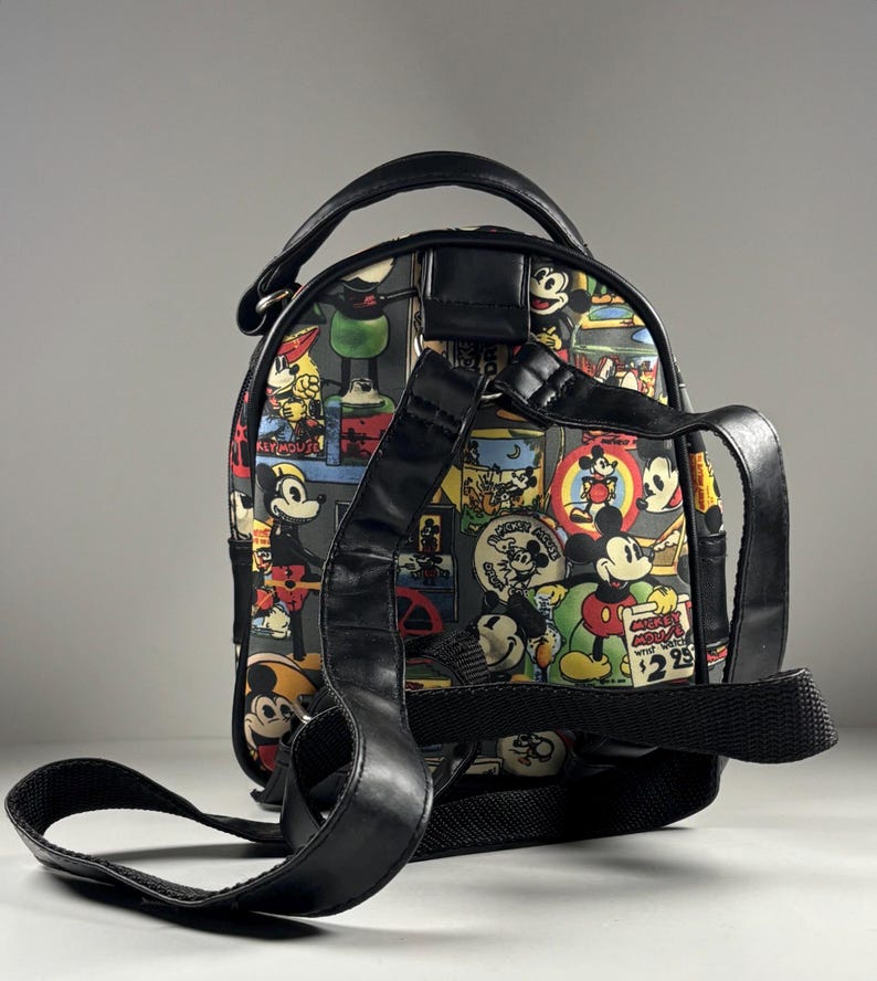 Puede incluir: Una mochila peque&ntilde;a con un estampado colorido de ilustraciones vintage de Mickey Mouse, que incluye el texto "Mickey Mouse wrist watch $2.95". La bolsa tiene correas, un asa superior y bordes negros, mostrada desde la parte posterior.