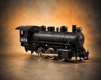 May include: A black model steam locomotive train with the number 3474 printed in white on the side of the cab. The engine features gold-colored metal wheels and connecting rods, a cylindrical boiler, a chimney, and a detailed cabin structure.