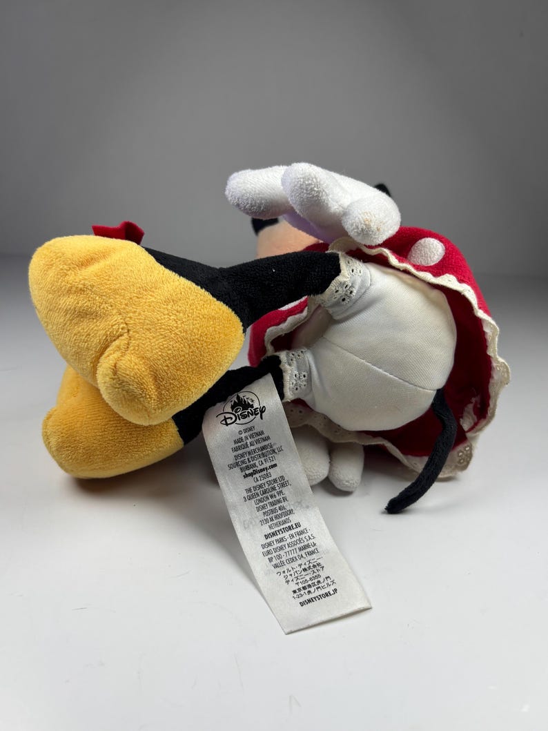 May include: A plush Minnie Mouse doll, lying on its side. The doll features a red and white polka-dot dress, white gloves, and yellow shoes. The tag reads "Disney".