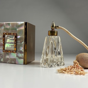 May include: An antique perfume bottle with a faceted glass design and a gold-colored metal top. A matching pear-shaped atomizer and a decorative box with a mother-of-pearl mosaic exterior are also present.
