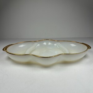Peut inclure: Un plat de service en verre blanc opalescent avec un design à trois sections. Le plat a un bord festonné et est bordé d'une bande dorée. Le plat est conçu pour servir des collations ou des apéritifs.