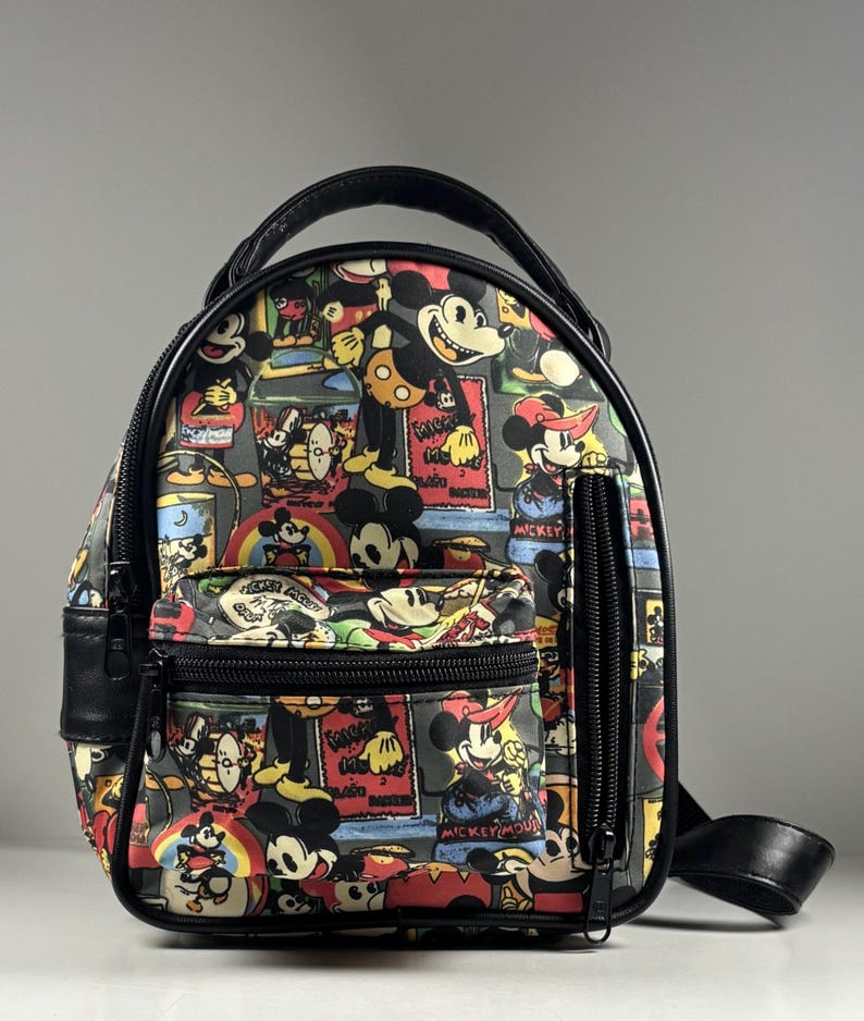 Puede incluir: Una mochila peque&ntilde;a con un estampado colorido de Mickey Mouse en varias poses y atuendos. La bolsa tiene bordes negros, un asa superior, un bolsillo frontal con cremallera y un bolsillo lateral vertical con cremallera en color negro.