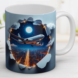 Puede incluir: Taza de cerámica blanca con un diseño azul y blanco. El diseño presenta un avión volando sobre una ciudad por la noche con una luna llena en el cielo.
