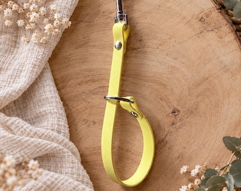 May include: A bright yellow wrist strap featuring a silver-toned metal swivel snap hook at the top and a silver metal ring connecting the loop. The strap is constructed from a smooth, solid-colored material and secured with silver metal rivets.