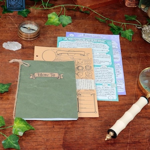May include: A selection of items on a wooden surface, including a green notebook with "How To" text, a magnifying glass, and printed papers. A compass, crystals, and decorative ivy are also present.