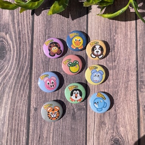 Pode incluir: Dez botões coloridos do Zoo Pals com diferentes rostos de animais. Cada botão tem as palavras "Zoo Pals" em uma faixa amarela no topo.