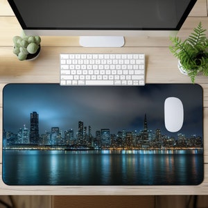 May include: A dark blue and black mouse pad with a cityscape skyline at night. The city is lit up with lights and reflected in the water below.