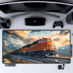 May include: A large orange and black freight train travels through a mountainous landscape. The train is moving through a snowy mountain pass with a cloudy sky in the background.