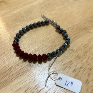 May include: A red and black beaded bracelet with a silver clasp. The bracelet has a price tag that says "12$".