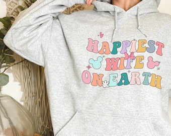 May include: Gray hooded sweatshirt with the text "Happiest Wife on Earth" in colorful letters with Mickey Mouse ears and a bow.