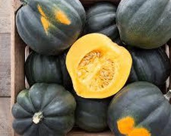 May include: A wooden crate filled with several dark green acorn squash. One squash is cut open, revealing bright orange flesh and seeds. Some squash have yellow markings. The crate sits on a light-colored wooden surface.