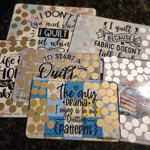 May include: A collection of rectangular quilting-themed cards with various quotes and designs. The cards feature phrases like "I quilt because fabric doesn't fall back" and "Life is short, buy fabric." Each card is decorated with gold or white polka dots.