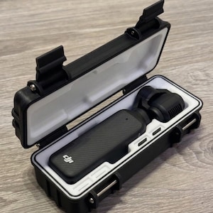 May include: Black protective case with a white interior, holding a black handheld camera. The case is open, revealing the camera and its components. The case has a secure latching mechanism and is designed for portability.