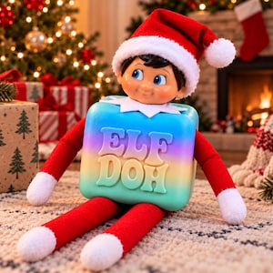 May include: A plush elf doll wearing a red hat with a white pom-pom and a white collar. The elf is attached to a square, gradient-colored block that transitions from blue to yellow and pink, featuring the embossed text ELF DOH on the front.