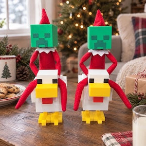 May include: Two plush dolls with red felt bodies and pointed hats, each wearing a green block-shaped mask with a pixelated face, sitting atop white block-shaped chicken figures with yellow beaks, red wattles, and yellow feet.