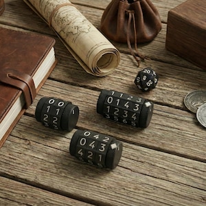 May include: A collection of tabletop gaming accessories on a wooden surface. Includes three black combination locks, a 20-sided die, coins, a leather-bound journal, a rolled map, a small leather pouch, and a wooden box.